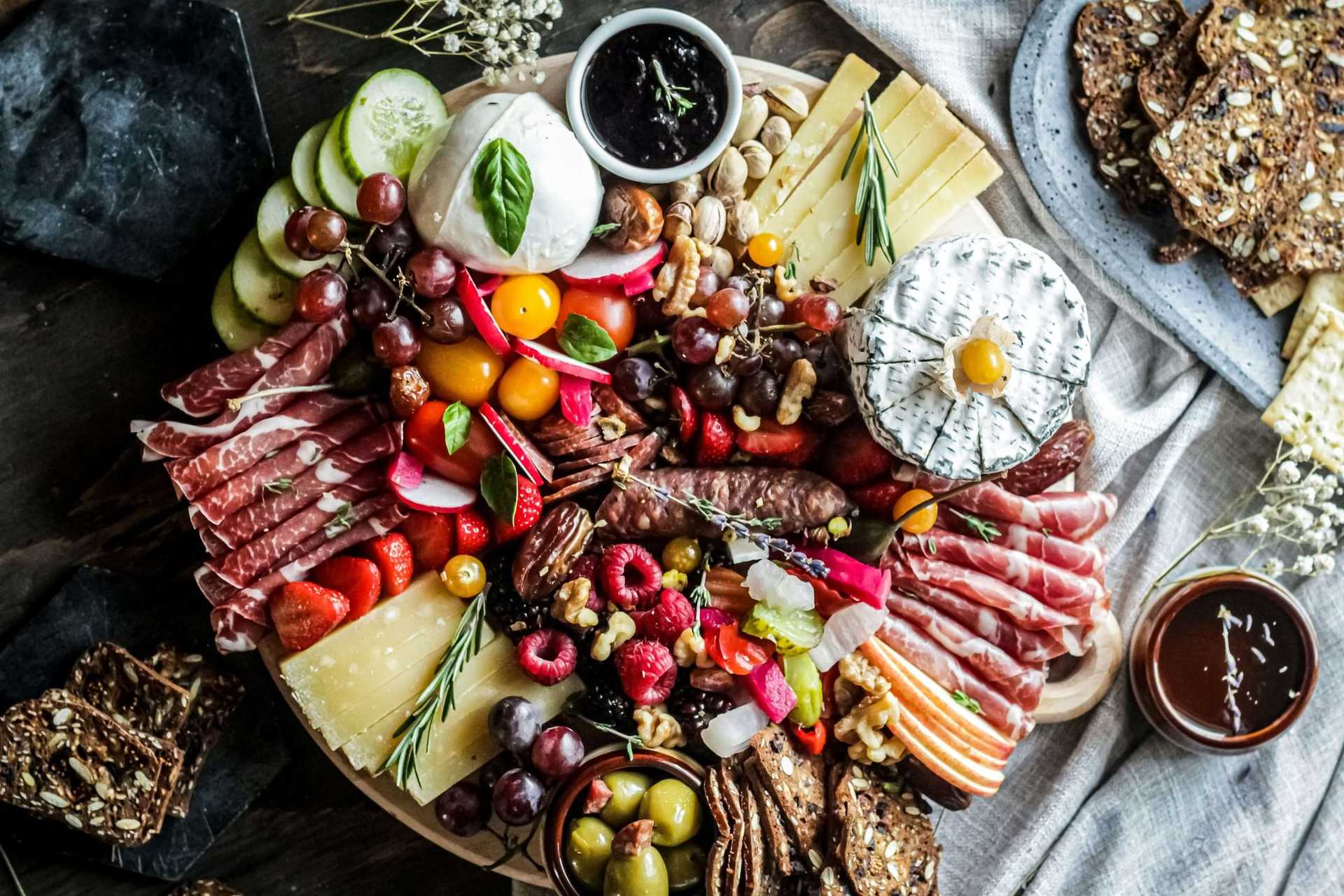 A vibrant charcuterie board with assorted cheeses, meats, fruits, nuts, and bread on a wooden platter.